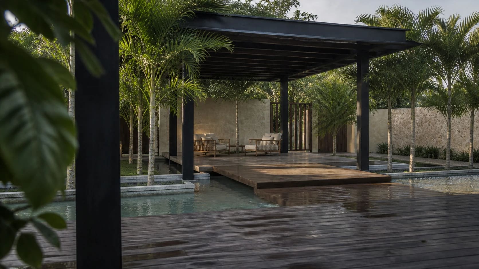 Pérgola de acero negro sobre un espejo de agua y andador, con piso de piedra mojada y palmeras alrededor.